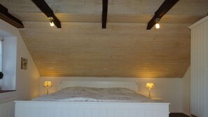 A bedroom with a wooden ceiling, a white bed, and two bedside lamps. - Villa Jonny am Deich (Dornum)