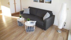 A modern living room with a dark grey sofa, two white round tables with metal frames, and a white floor lamp. - In the Villa Granitz (Göhren)