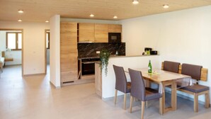 A modern kitchen with wooden cabinets, a marble countertop, and a dining area with a wooden table and chairs.
