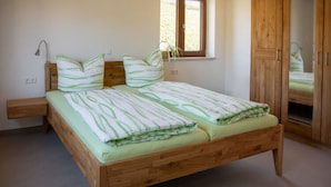 A wooden bed with green and white striped bedding, a bedside table, and a window with a view of greenery.