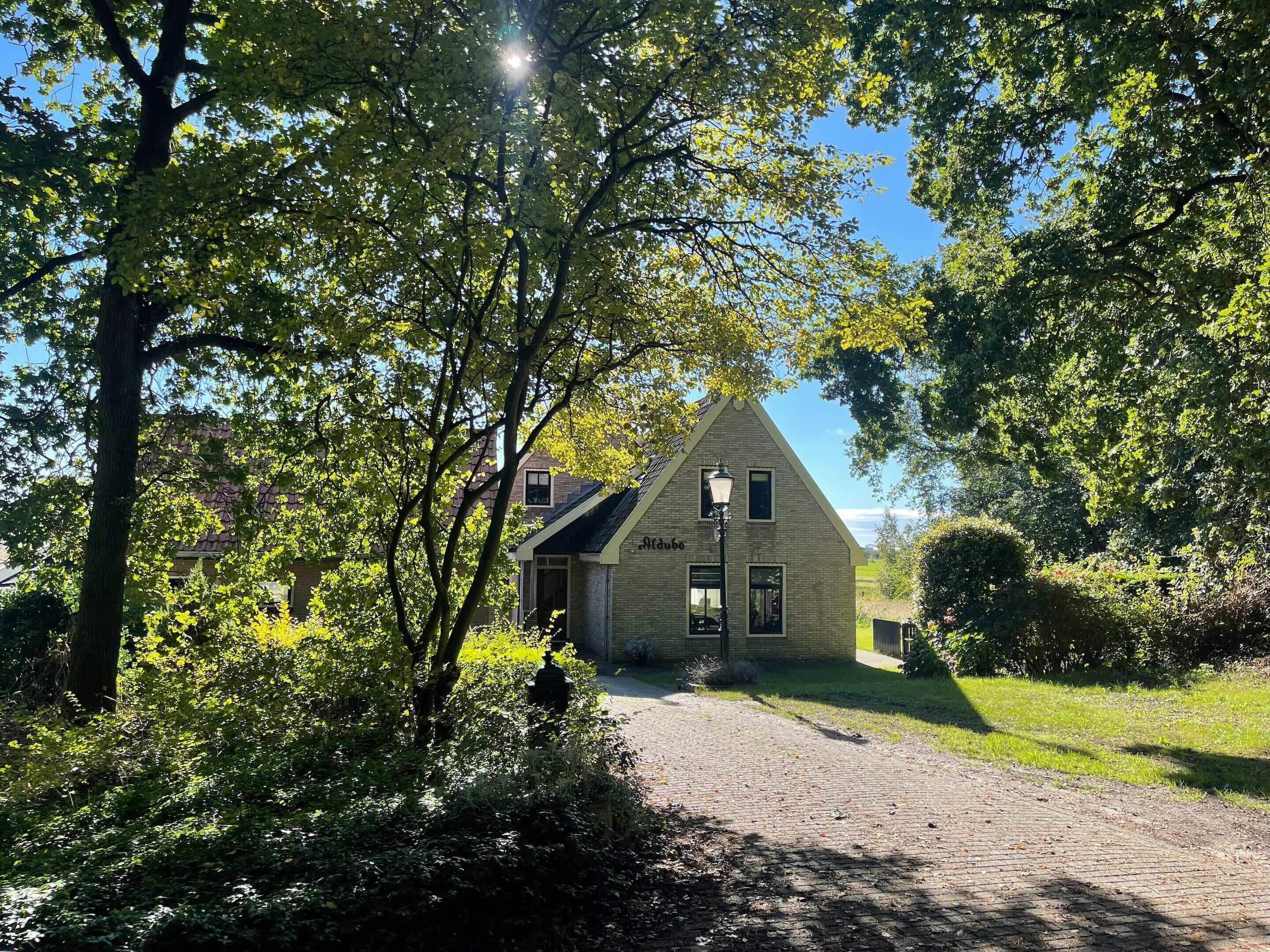 A traditional house with a sloped roof, a visible chimney, and a paved driveway leading to the entrance.