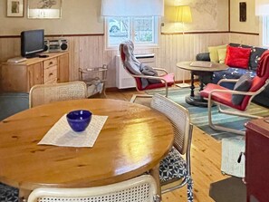A cozy living room with a wooden table, a blue bowl, a television, a radio, and a sofa with colorful cushions.