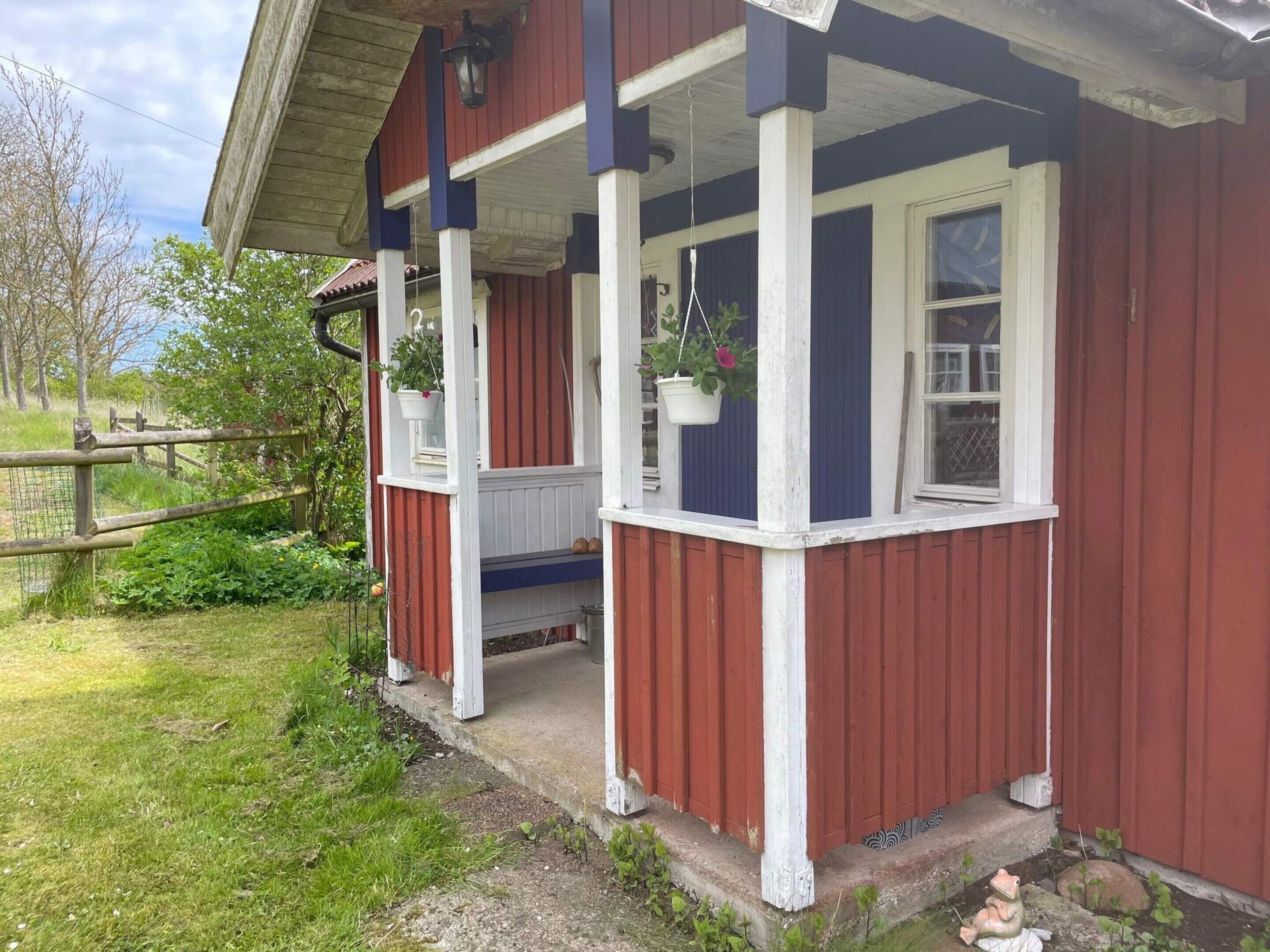 A red and white building with a porch, a wooden fence, and greenery.