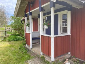 A red and white building with a porch, a wooden fence, and greenery. - 4 Star Holiday Home in Ronneby (Ronneby)