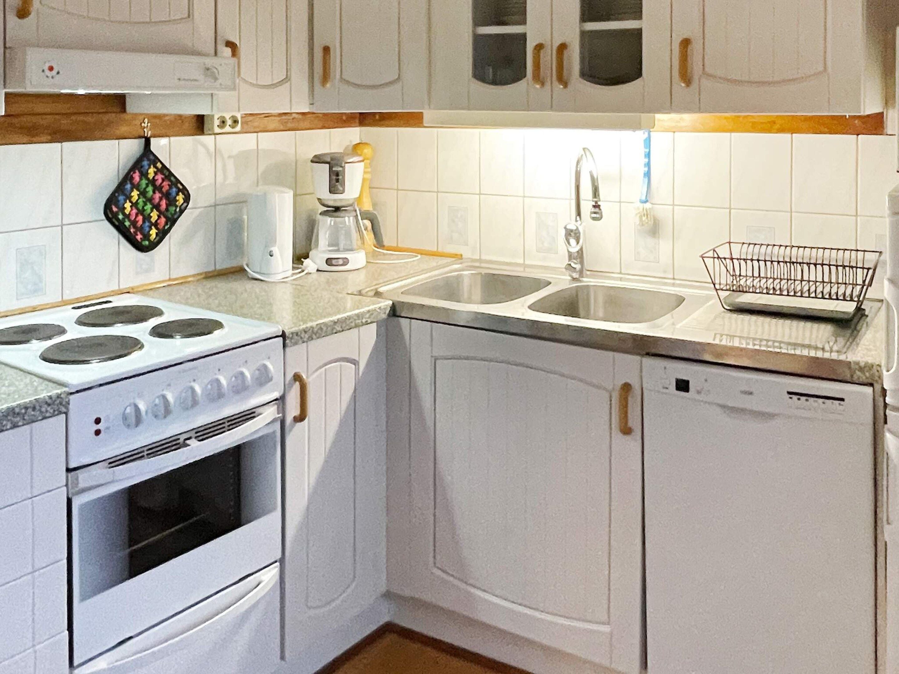 Une cuisine avec des meubles blancs, une cuisinière, un évier et une machine à café.