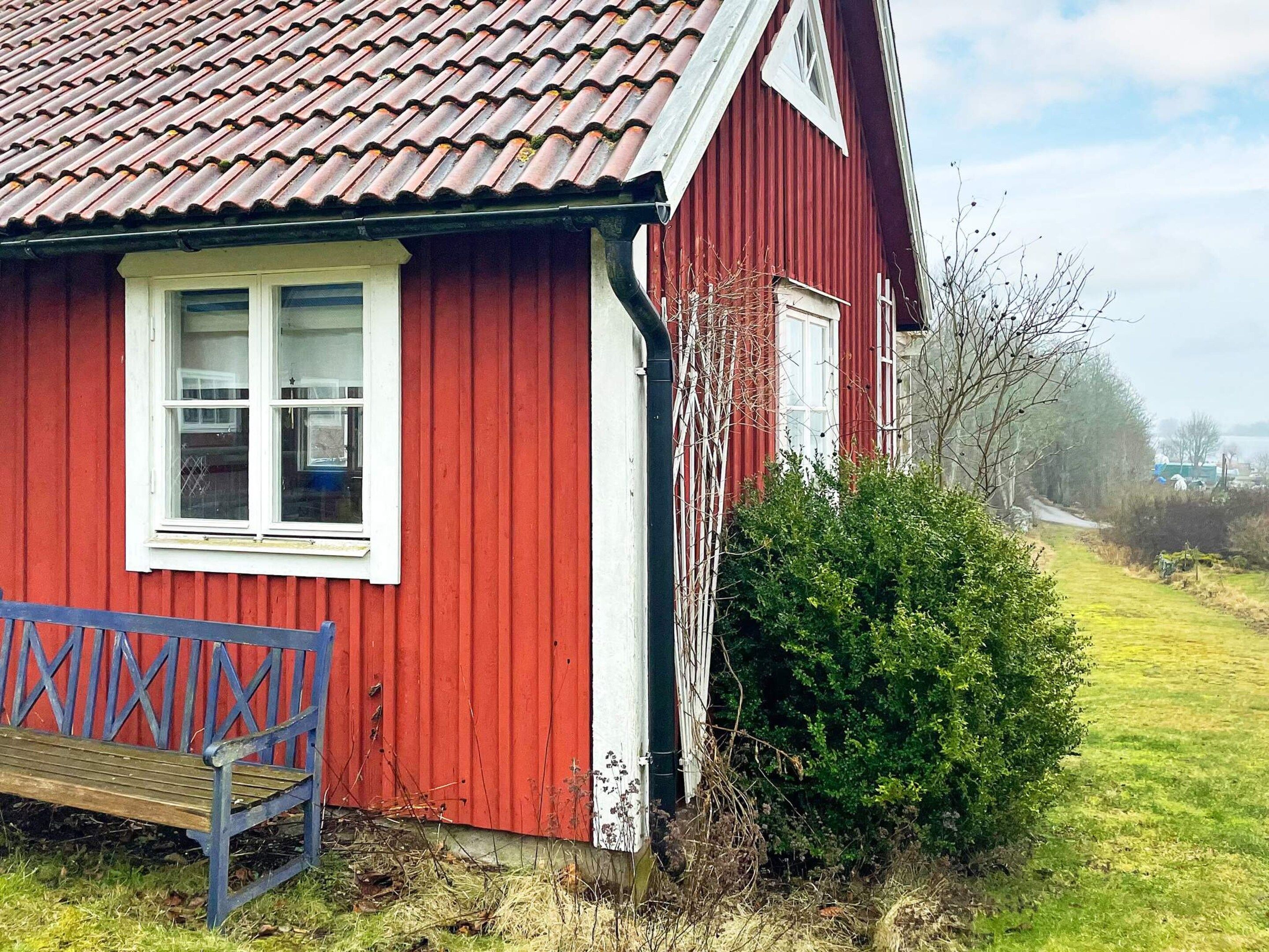 Un bâtiment rouge avec un toit en tuiles, un banc et un arbuste vert au premier plan.