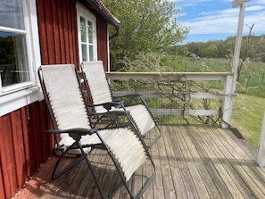 Une terrasse en bois avec deux chaises longues et une fenêtre donnant sur un paysage verdoyant.