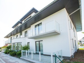 En moderne bygning i to etager med en hvid facade, store vinduer og en altan med glasgelændere.