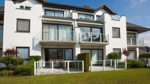 Un edificio residencial moderno de dos pisos con amplios ventanales, balcones y un césped bien cuidado.