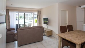 Una sala de estar con sofá, televisor, mesa de comedor con sillas y balcón con cortinas.