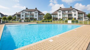 Un área de piscina con un suelo de ladrillo, rodeada de edificios modernos de dos pisos con balcones.