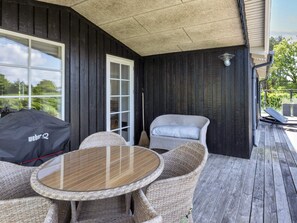 A covered outdoor seating area with wicker furniture, a glass table, and a Weber grill. - 4 Star Holiday Home in Hadsund (Hadsund)