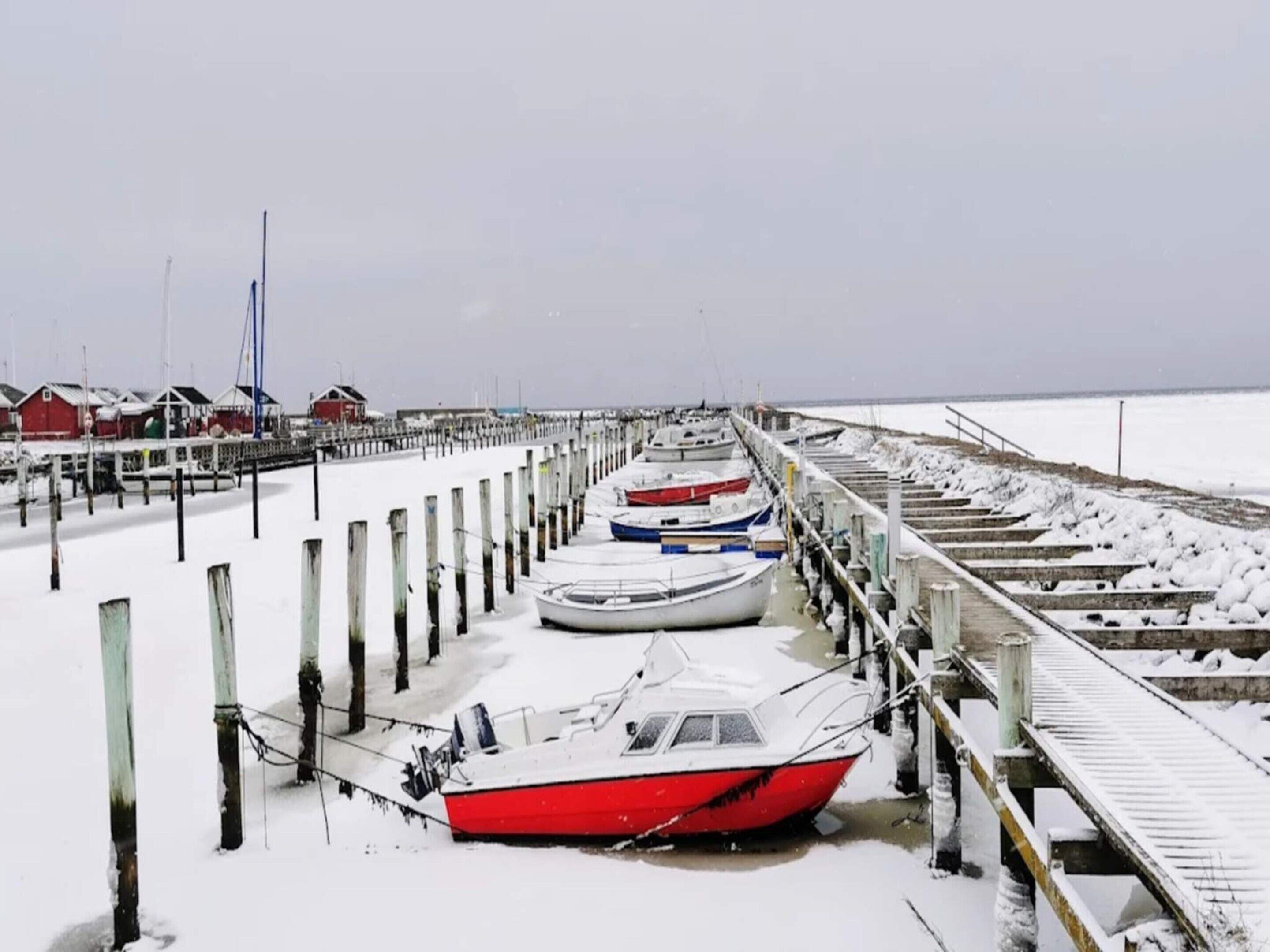 A pier with boats docked, wooden posts, and a snowy landscape.