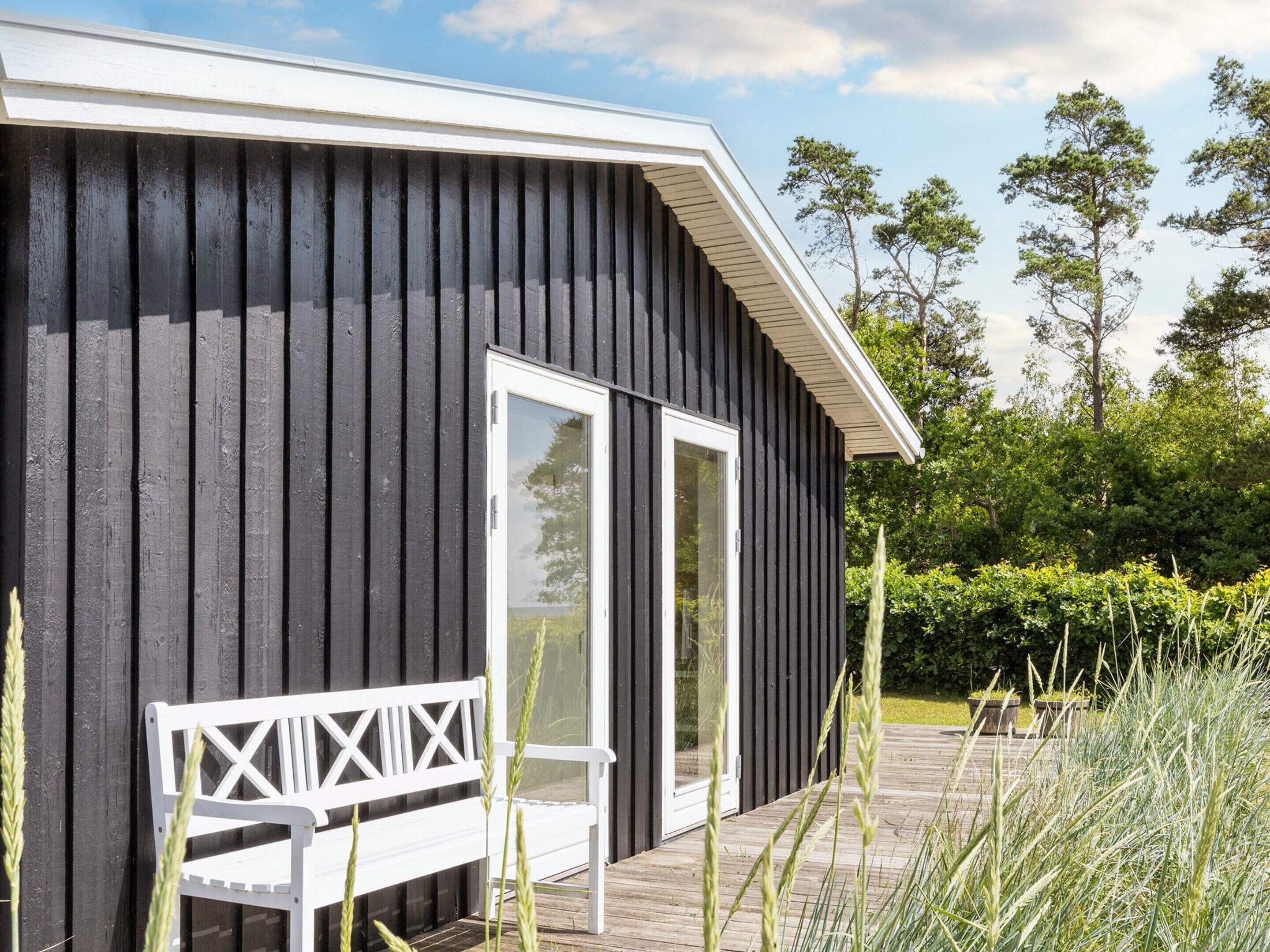 A black wooden building with a white door and a white bench outside.