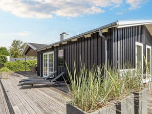 A modern house with a wooden deck, a covered outdoor seating area, and a garden with tall grasses. - 4 Star Holiday Home in Hadsund (Hadsund)