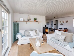 A cozy living room with a fireplace, white sofas, a coffee table, and a dining area in the background.
