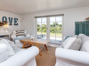 A room with a white sofa, a wooden coffee table, and a large window with a view of greenery.