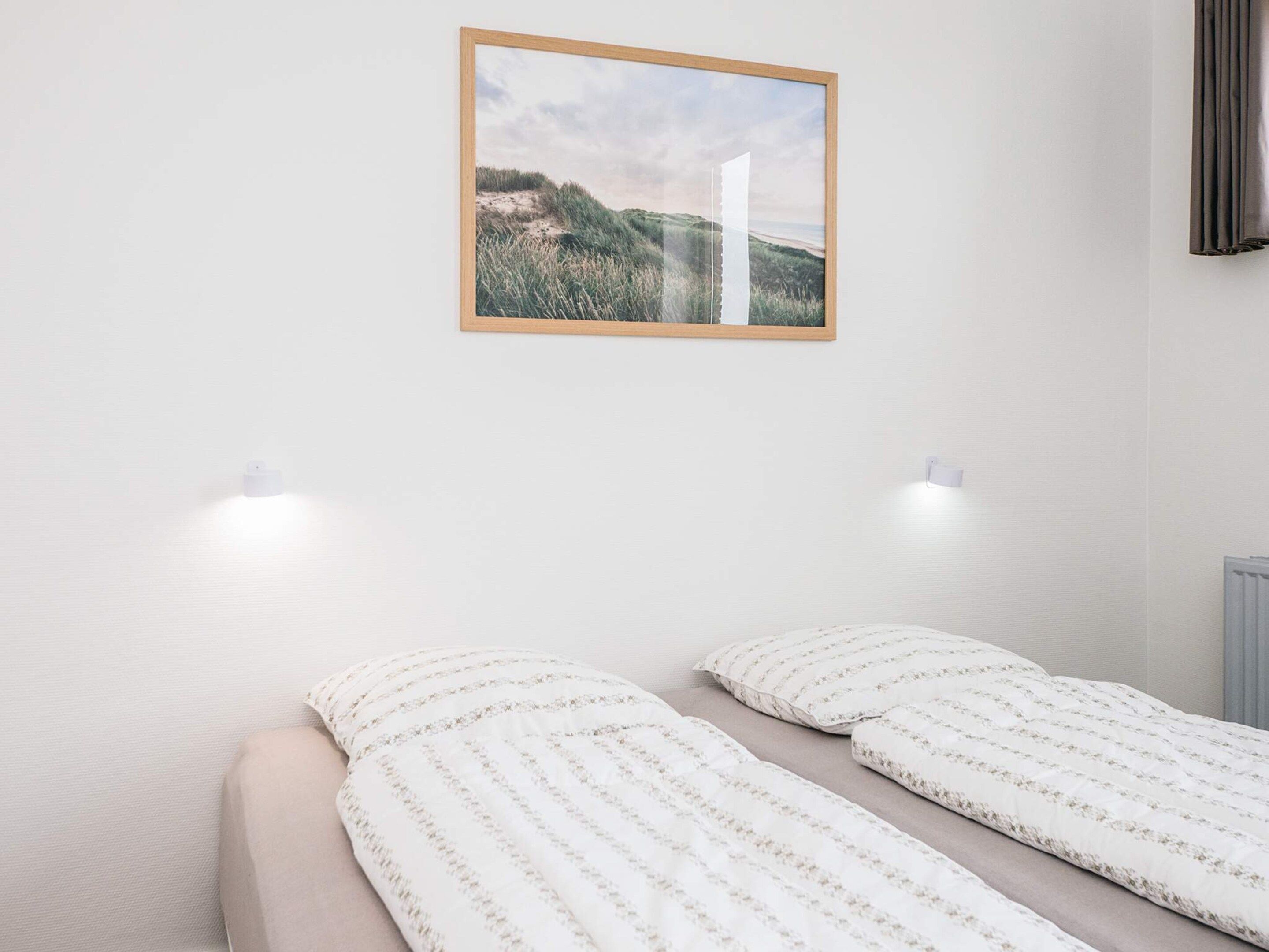 Un dormitorio con una cama, dos luces fijadas a la pared y un cuadro enmarcado.
