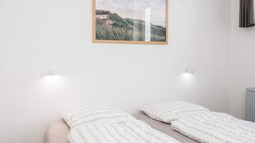 Un dormitorio con una cama, dos luces fijadas a la pared y un cuadro enmarcado.