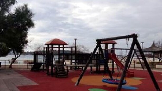 A playground with swings and slides, a covered seating area, and a red carpeted ground. - Apartment Mijatovic (Vodice)