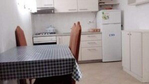 A compact kitchen with white cabinets, a small refrigerator, and a table with a checkered tablecloth. - Apartment Mijatovic (Vodice)