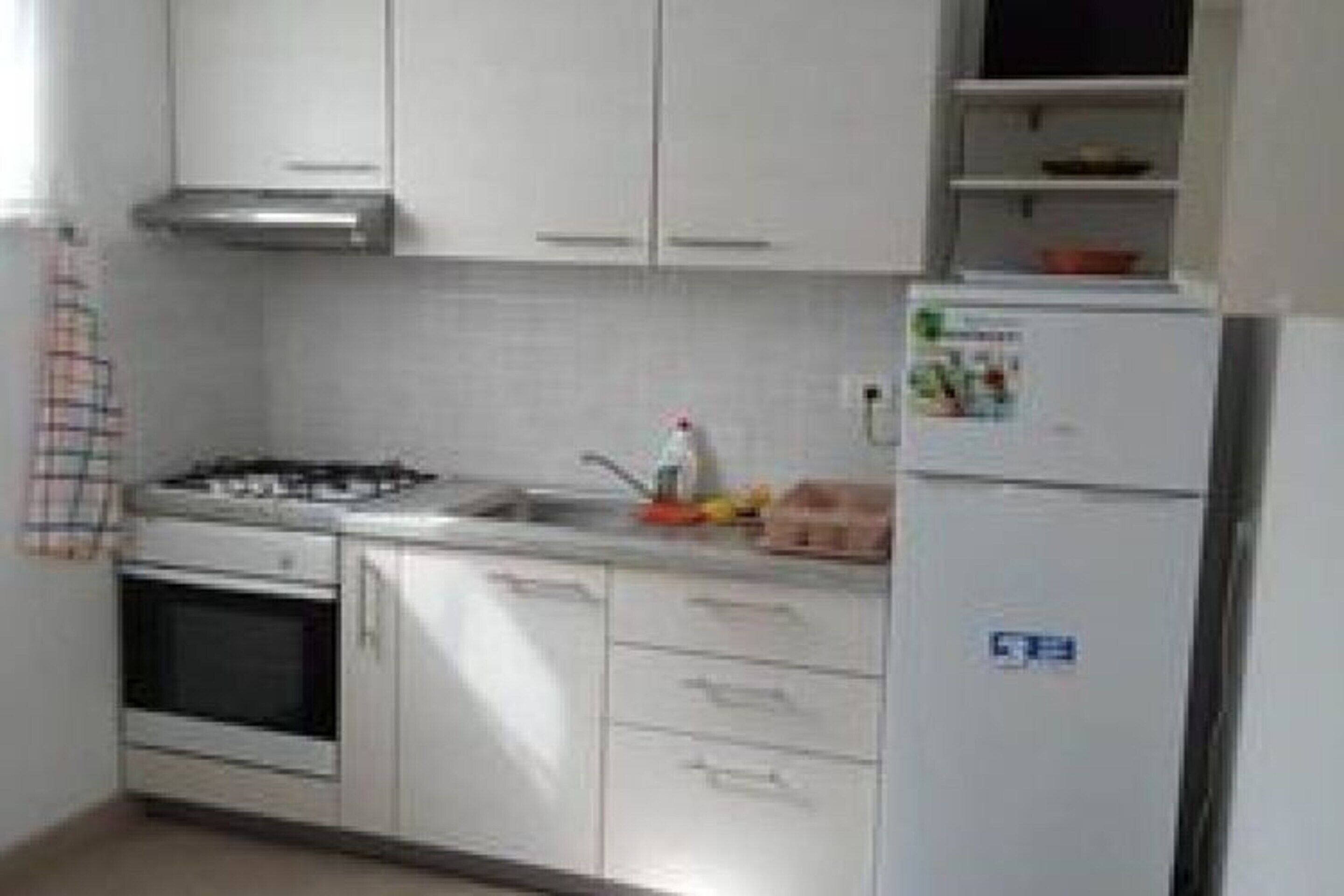 Una cocina con armarios blancos, estufa, fregadero y refrigerador.