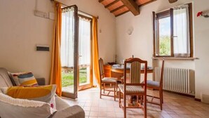 A room with a sofa, a dining table with chairs, a radiator, and a window with curtains. - Holiday Home in Urbania With Garden BBQ (Urbania)