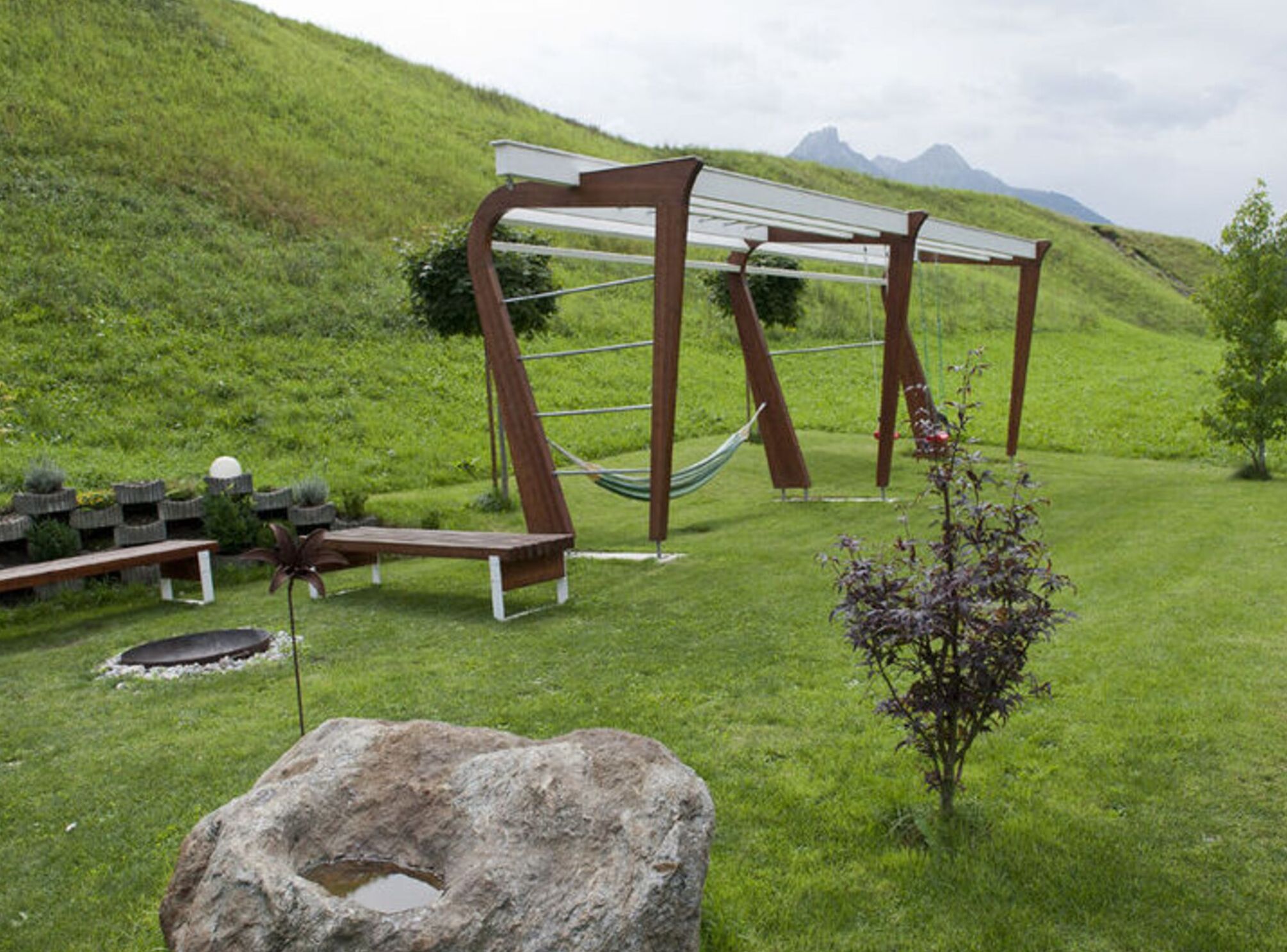 A grassy outdoor area with a hammock, benches, and a rock.