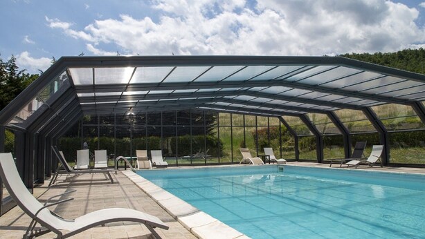 An indoor swimming pool with a glass roof, surrounded by lounge chairs and a tiled floor. - Holiday Home in Trivigno With Pool and Garden (Trivigno)