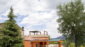 A building with a stone facade, a covered patio with outdoor seating, and a view of mountains in the background. - Holiday Home in Trivigno With Pool and Garden (Trivigno)