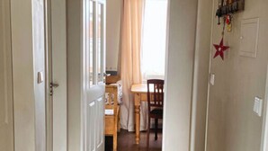 A hallway with wooden flooring, white walls, and a door leading to a room with a bed and a window. - Bunte Kuh Comfortable Holiday Residence (Borkum)