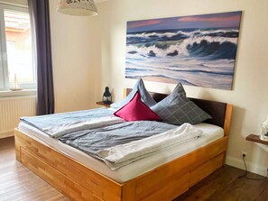 Una camera da letto con un letto di legno, un comodino, una lampada e un quadro raffigurante onde sulla parete.