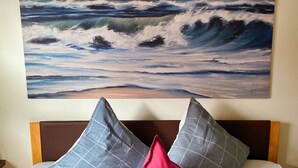 A bedroom with a large ocean painting on the wall, a bed with a wooden headboard, and two pillows. - Bunte Kuh Comfortable Holiday Residence (Borkum)