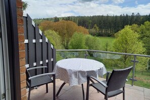 Un balcon avec une table ronde et deux chaises, donnant sur une zone boisée.