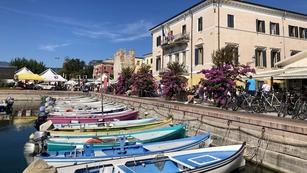 A waterfront with colorful boats docked, a building with a balcony, and a clear blue sky. - Perlago Comfortable Holiday Residence (Costermano sul Garda)