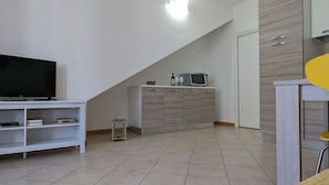 A modern living room with a flat-screen TV on a white TV stand, a small cabinet with a microwave, and a yellow chair. - Perlago Comfortable Holiday Residence (Costermano sul Garda)