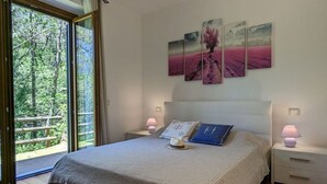 A bedroom with a large bed, a view of trees through a sliding glass door, and a wall with three paintings. - Perlago Comfortable Holiday Residence (Costermano sul Garda)
