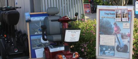 A mobility scooter parked in front of a building with a signboard and a sign indicating a nearby location.