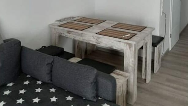 A dining area with a rustic wooden table, grey sofa, and pendant lights. - Holiday Apartment Cabin 2c (Norden)