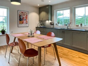 A modern kitchen with grey cabinets, a wooden dining table with pink placemats, and a large window providing a view of greenery outside. - 5 Star Holiday Home in Lottorp (Löttorp)