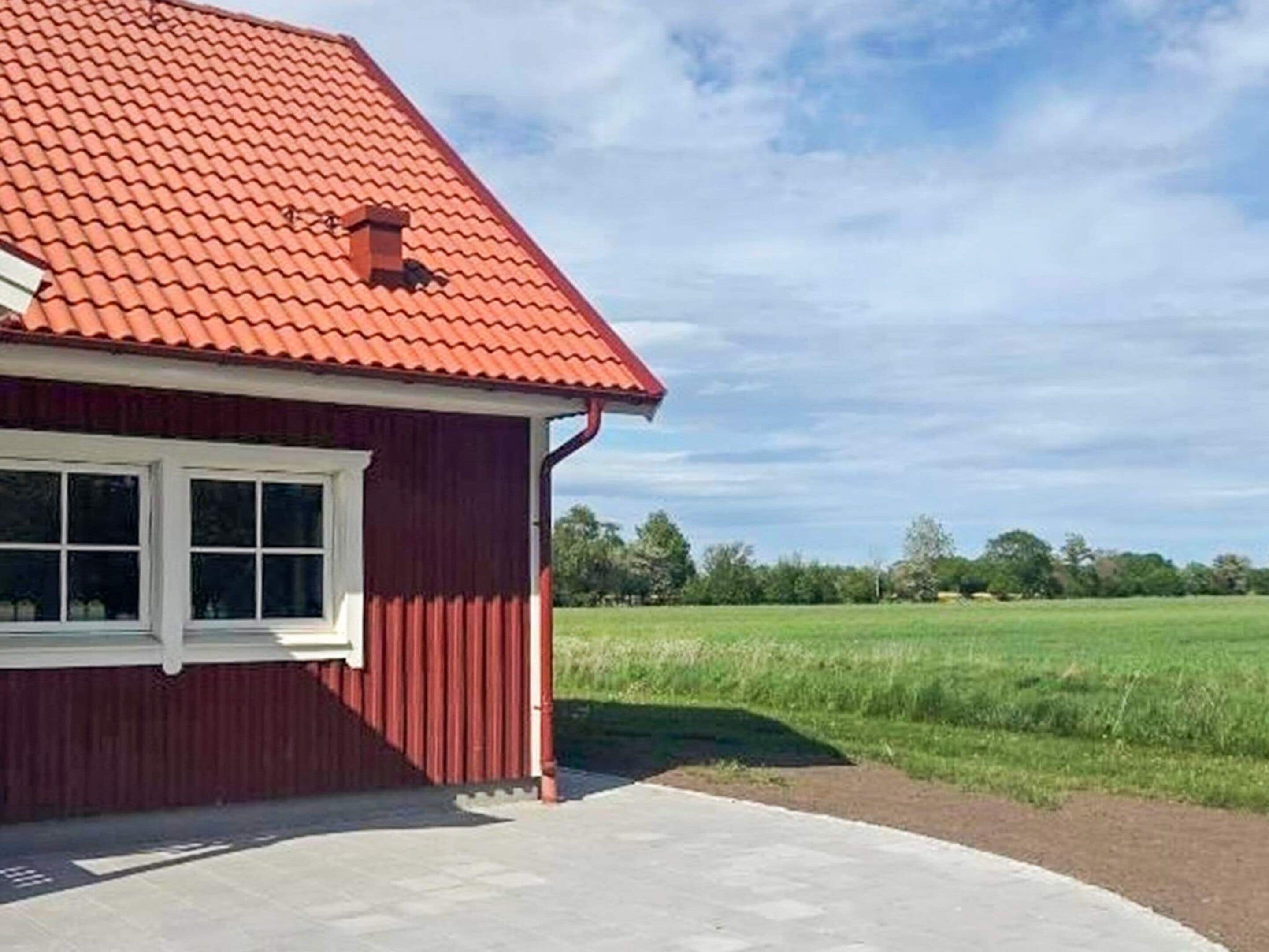 Un bâtiment rouge avec un toit en pente, une fenêtre et une zone pavée devant.