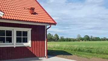 A red building with a sloped roof, a window, and a paved area in front.