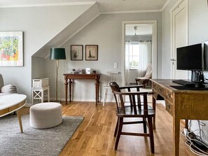 Una habitación con un escritorio de madera, una silla, una lámpara, un televisor y un ventanal con cortinas.