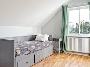 A bedroom with a sloped ceiling, a bed with patterned bedding, a bedside table with a lamp, and a window with curtains. - 5 Star Holiday Home in Lottorp (Löttorp)