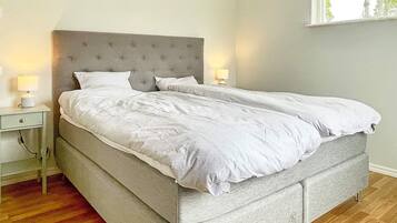 A neatly made bed with a grey headboard, two bedside lamps, and a wooden floor.
