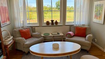 Una sala de estar acogedora con dos sofás, una mesa redonda y vistas a un campo verde a través de amplios ventanales.