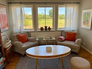 A cozy living room with two sofas, a round table, and a view of a green field through large windows. - 5 Star Holiday Home in Lottorp (Löttorp)
