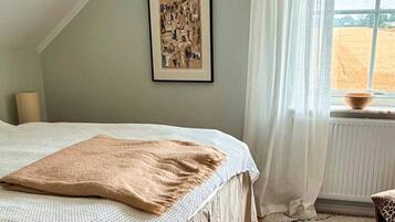 Un dormitorio con cama, un cuadro en la pared, una ventana con vistas a un campo y un radiador.