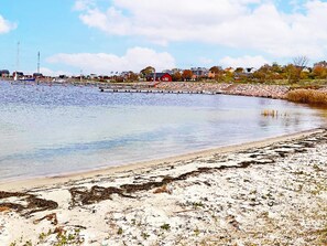 A coastal area with a sandy beach, a calm body of water, and a row of houses in the background. - 5 Star Holiday Home in Lottorp (Löttorp)