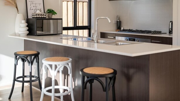 A modern kitchen with a central island, bar stools, a stainless steel sink, and a gas stove. - Modern new Homly House at Clyde (Clyde)